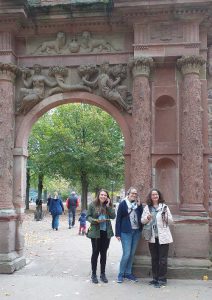3 Frauen mit Audioguides stehen an einem steinernen Tor mit verzierten Säulen und Skulpturen 