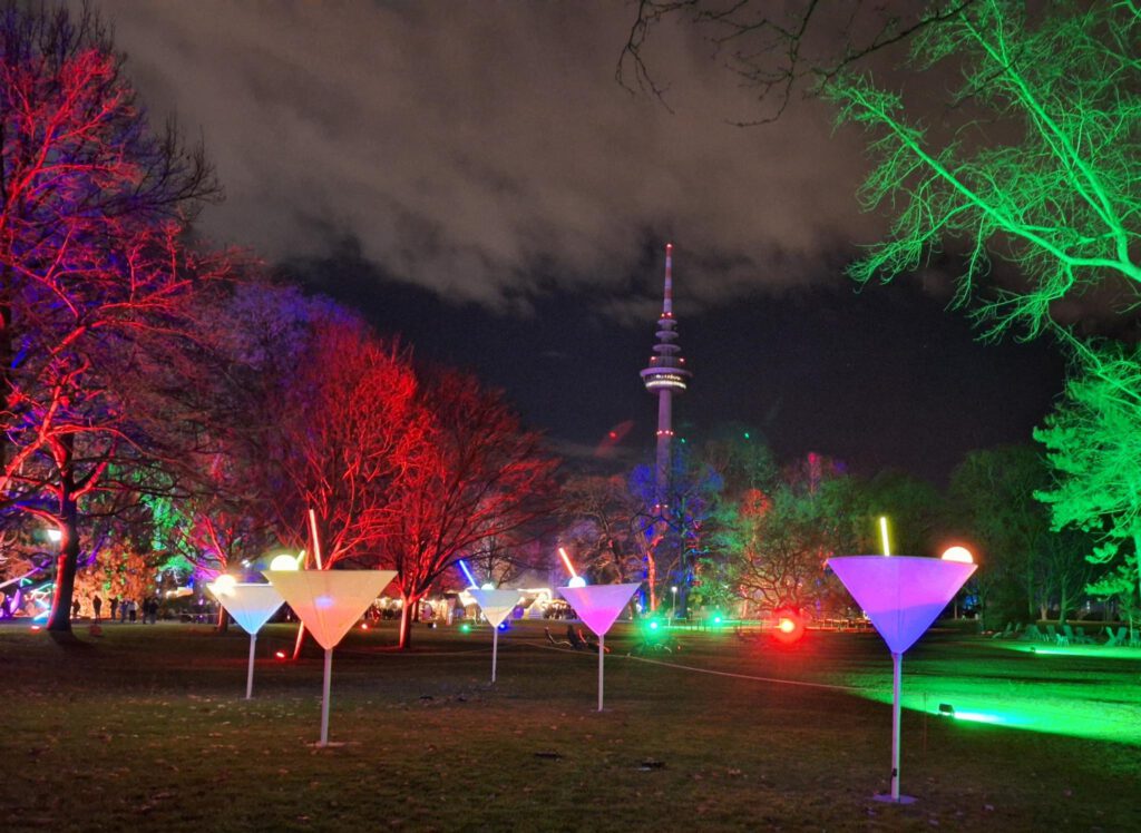 nächtlich beleuchtete große Cocktailgläser auf einer Wiese vor dem Fernsehturm